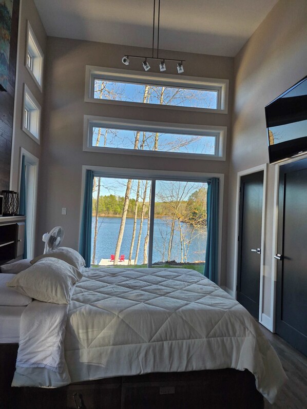A bedroom with a large bed, a fan, and a view of a lake.