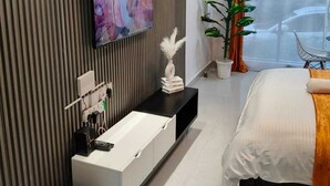 Een moderne hotelkamer met een groot bed, een televisie bevestigd aan een lattenwand, een nachtkastje met een witte vaas en een potplant.
