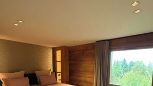 Een moderne slaapkamer met een groot bed, een bankje, een raam met uitzicht op bomen en houten wanden.