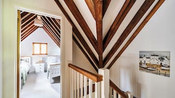 Eine Treppe mit Holzbalken und weißen Geländern führt zu einem Schlafzimmer mit Bett und Fenster.