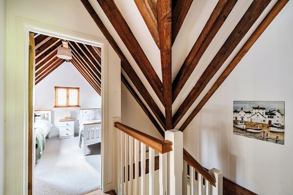A staircase with wooden beams and white railings leading to a bedroom with a bed and a window.