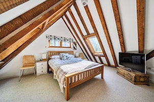A bedroom with a sloped ceiling, a wooden bed, a TV, and a window.