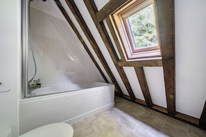 Een badkamer met een bad, een douche en een raam.