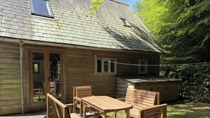 Une cabane en bois dotée d’un patio comprenant une table et des chaises, un petit abri de jardin et une fenêtre.