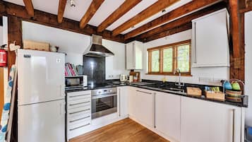 Una cocina con armarios blancos, un refrigerador de acero inoxidable, un horno empotrado y una ventana con persianas.