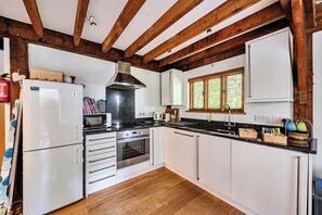 Una cocina con armarios blancos, un refrigerador de acero inoxidable, un horno empotrado y una ventana con persianas.
