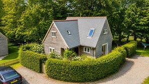 A two-story house with a sloped roof, surrounded by a well-maintained hedge, and a gravel driveway.