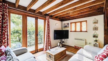 A cozy living room with wooden beams, a large TV, and a fireplace.