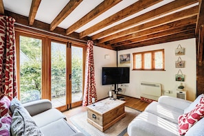 Een gezellige woonkamer met houten balken, een grote televisie en een open haard.