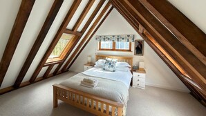 Une chambre avec un plafond en pente, un lit en bois, une table de chevet et une fenêtre donnant sur un beau paysage.