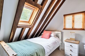 Un dormitorio con techo inclinado, una cama con edredón acolchado, una mesita de noche con lámpara y una ventana con persianas de madera.