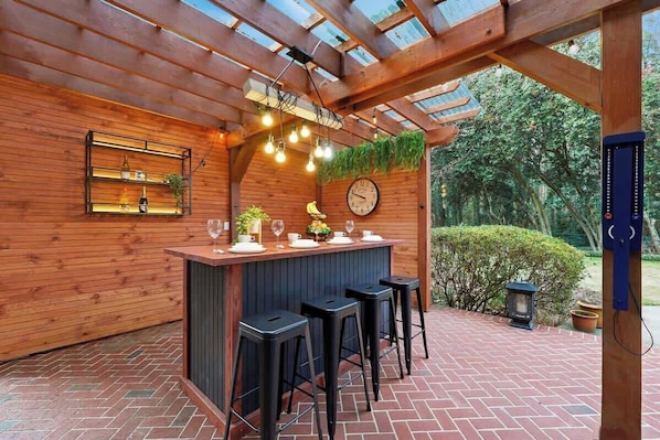 A wooden bar area with a clock, bar stools, and a brick floor.