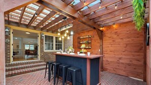 Un’area patio coperta con un bancone bar, sgabelli e luci a sospensione.