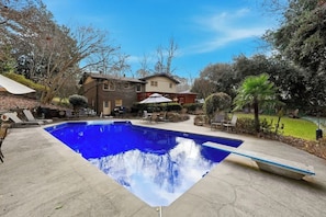 A swimming pool with lounge chairs, a house, and surrounding greenery.