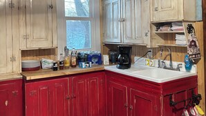 Una cocina con armarios de madera, encimera roja, cafetera y ventana con vista a árboles.