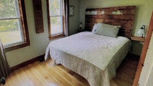 Un dormitorio con cama, mesita de noche, ventana y puerta.