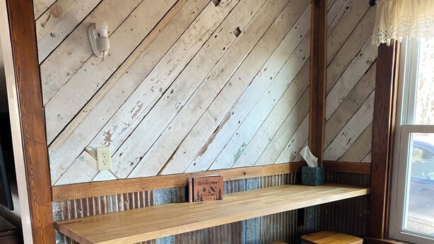 Un interior rústico con un banco y taburetes de madera, techo de madera y una ventana con vistas.