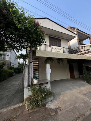 A two-story building with a balcony, a garage door, and a small garden area with plants.