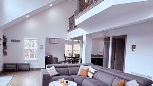 Uma sala de estar moderna com um sofá modular cinza, uma mesa de centro redonda e uma varanda com guarda-corpo.