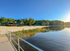 Una propietat a la vora d'un llac amb una platja de sorra, un moll i un edifici amb teulada verda.