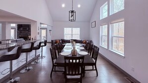 Uma área de refeições moderna com uma mesa comprida, banquetas de bar e grandes janelas.
