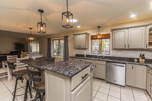 A modern kitchen with a central island, bar stools, pendant lighting, and a dishwasher.