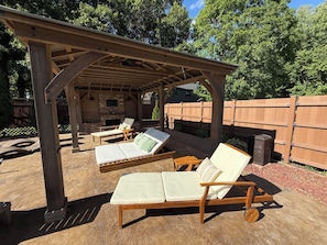 A covered outdoor seating area with lounge chairs and a stone fireplace.