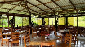 Un'area pranzo coperta con tavoli e sedie in legno, ampie finestre e vista sul verde.
