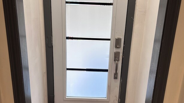 Un corridoio stretto con una porta bianca, vetri traslucidi e una maniglia. Il pavimento è rivestito di piastrelle decorate.
