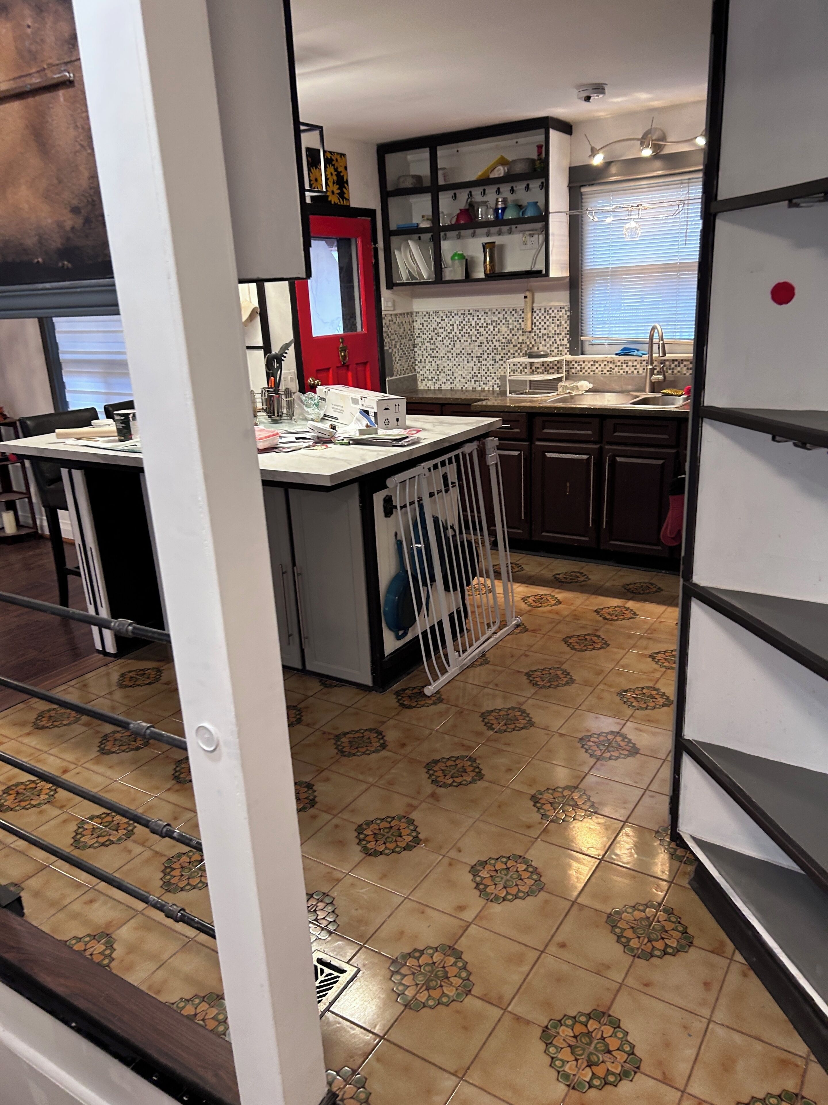 A kitchen with a tiled floor, a red door, and a white refrigerator.
