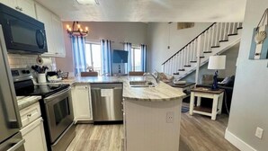 Una cucina moderna con elettrodomestici in acciaio inossidabile, un'isola centrale e una scala che conduce a una zona living.