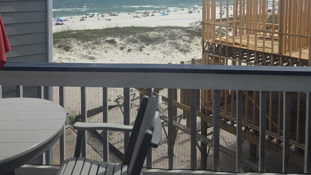 Un terrazzo con tavolo e sedie, affacciato su una spiaggia con una recinzione in legno e vista sull'oceano.