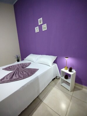 A bedroom with a bed, a nightstand, a lamp, and wall art.