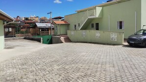 Un pati pavimentat amb una escala que condueix a un edifici de façana verda i un cotxe a prop.