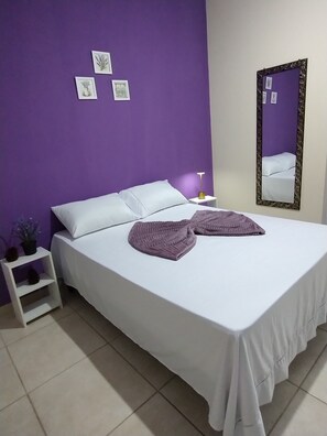 A bedroom with a bed, a nightstand, a mirror, and wall art.