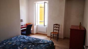 Une chambre à coucher comprenant un lit, un bureau, une chaise, un radiateur et une fenêtre donnant sur un paysage agréable.