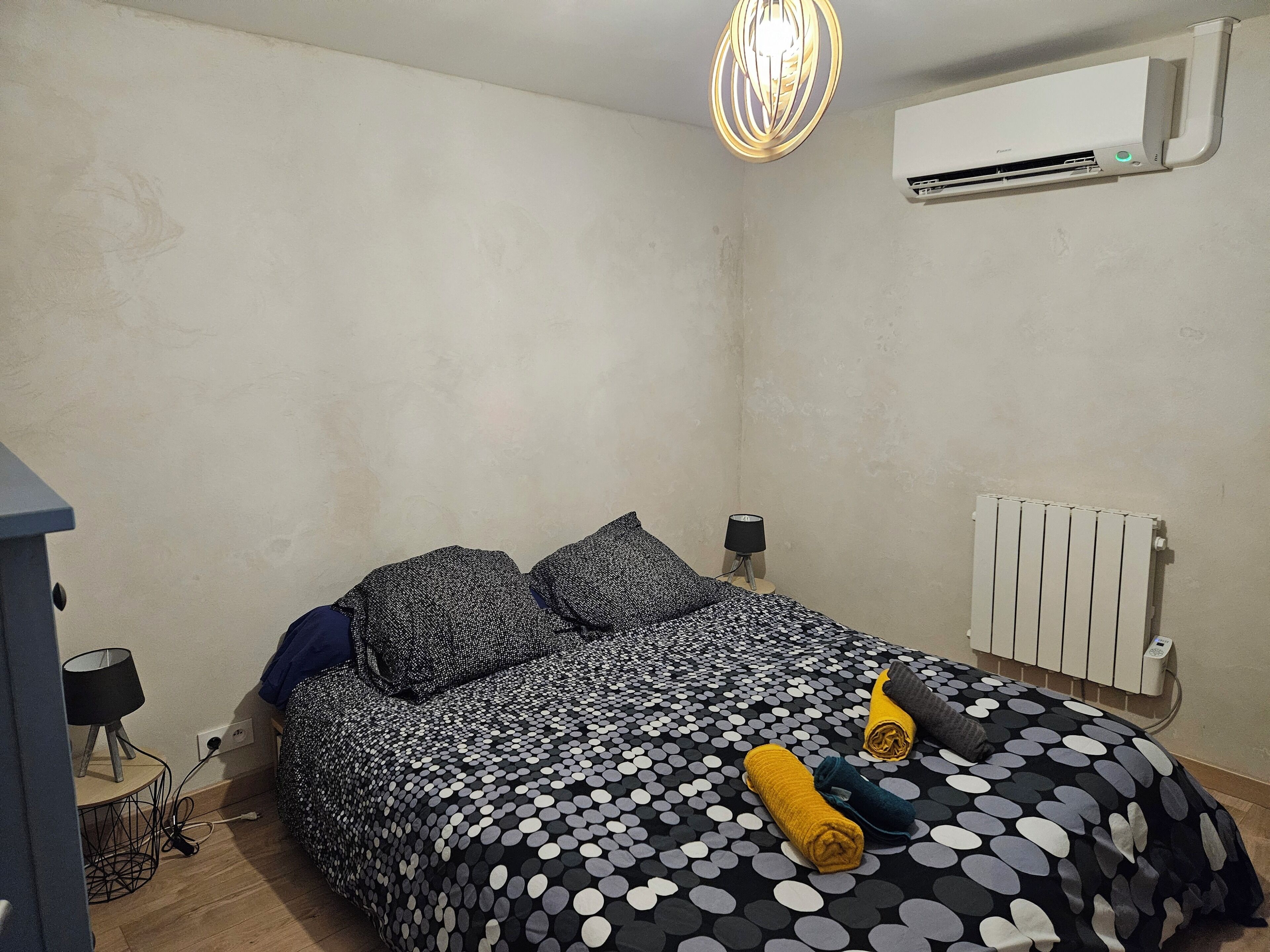 Une chambre à coucher avec un lit, un radiateur, un climatiseur fixé au mur et une lampe sur une table de chevet.