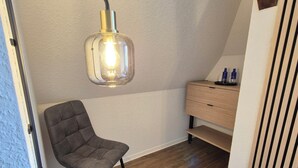 Una habitación con una silla, un escritorio, una lámpara y suelo de madera.