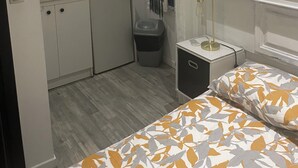 A compact room with a kitchenette, a bed with patterned bedding, and a small bedside table. - INICE  (Nice)