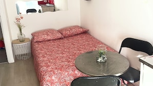 A compact room with a bed, a round table, two chairs, a small side table, and a mirror on the wall. - INICE  (Nice)