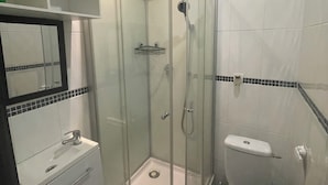 A bathroom with a glass-enclosed shower, a toilet, a sink with a mirror, and a tiled backsplash. - INICE  (Nice)