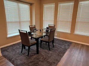 A dining area with a glass table, four chairs, and a rug.