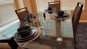 Une table à manger avec des chaises, de la verrerie et des bols noirs, le tout préparé pour un repas.