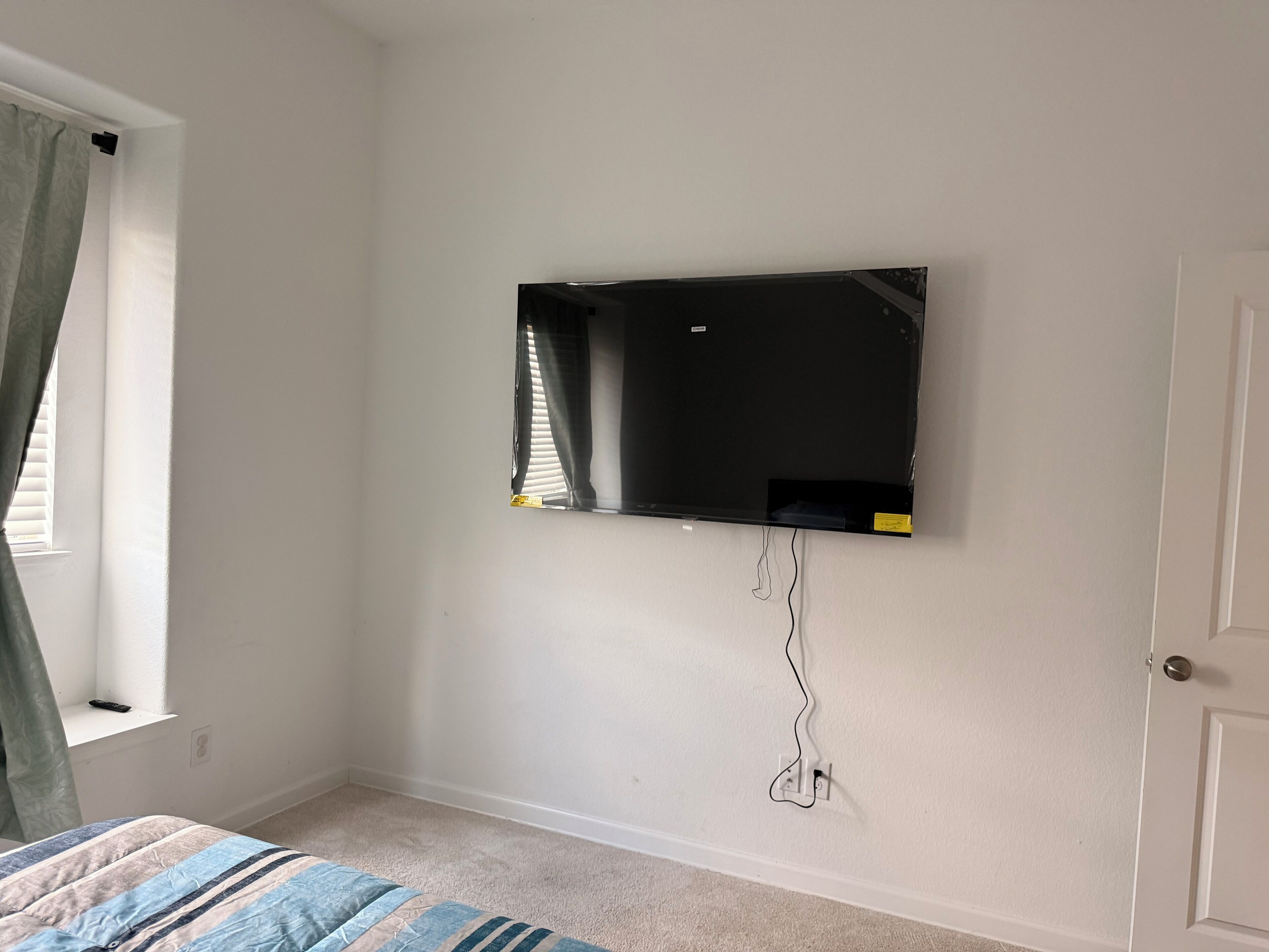 A bedroom with a bed, a wall-mounted TV, and a door.
