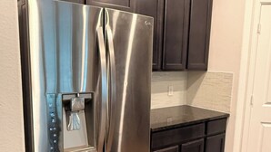 Un réfrigérateur en acier inoxydable doté d’un distributeur d’eau, de meubles de cuisine en bois foncé et d’une porte blanche.