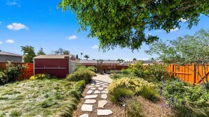 A garden pathway with stepping stones, surrounded by various plants and a wooden fence. - The Wild Flower by Coastline Vacation Rentals (San Diego)