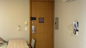 Camera d'albergo con porta in legno, una scrivania, una sedia, un telefono, un interfono e un condizionatore d'aria.