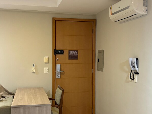 Une chambre d’hôtel avec une porte en bois, un bureau, une chaise, un téléphone, un système d’interphone et un appareil de climatisation.