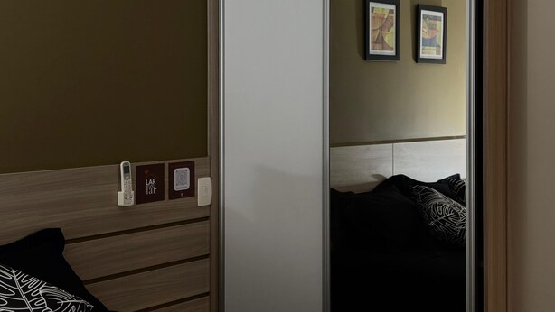 Una stanza con un letto, un armadio e uno specchio che riflette un letto e due quadri appesi al muro.