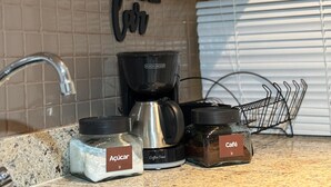 Un piano di lavoro in cucina con una macchina da caffè, un barattolo di zucchero e un barattolo per le spezie etichettato 'Café'.